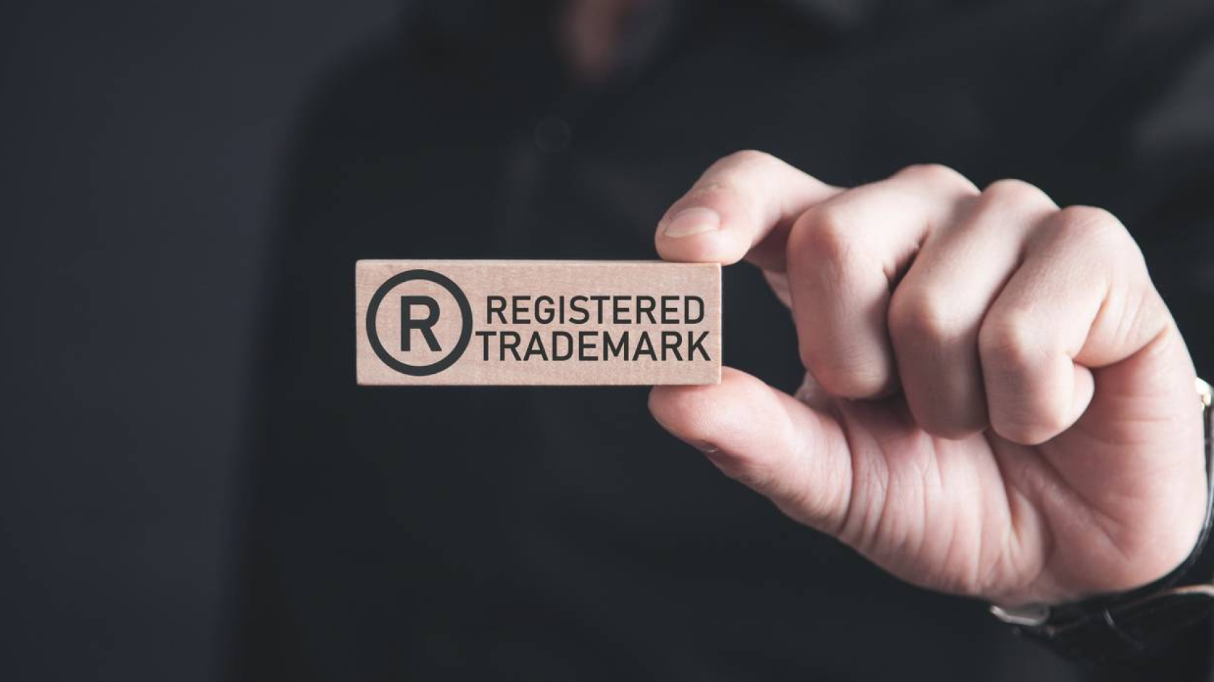 Male hand showing R-Registered trademark on wooden block.